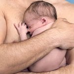 Particolare di uomo a torso nudo che abbraccia neonato