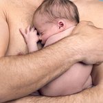 Particolare di uomo a torso nudo che abbraccia neonato